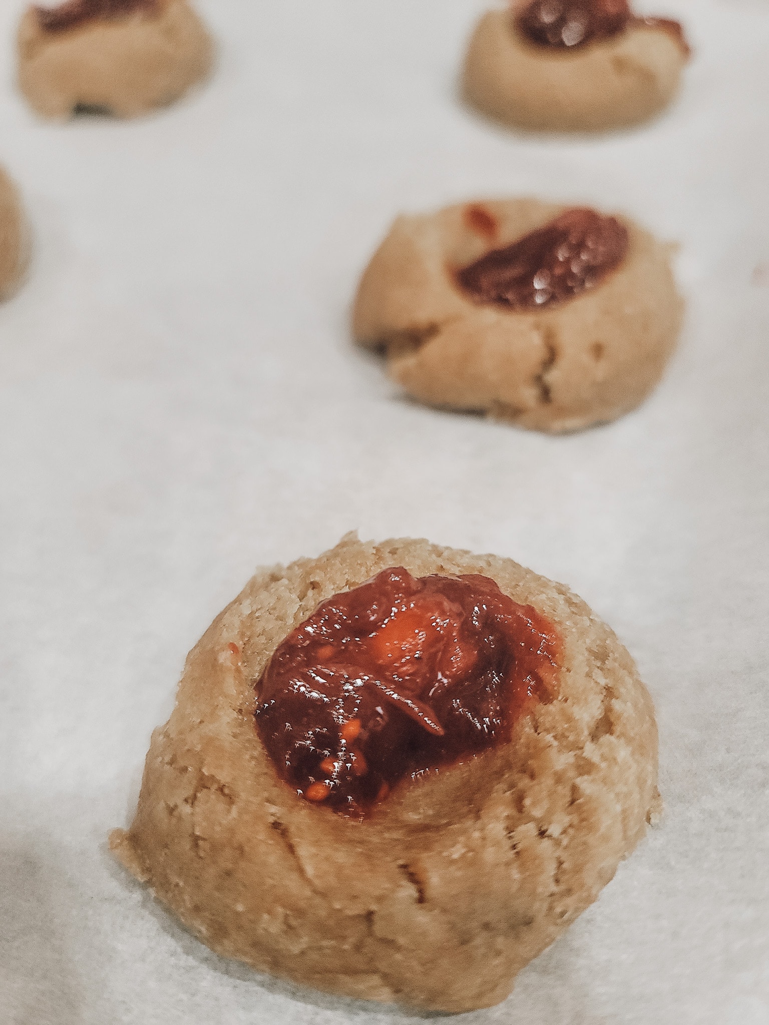 Place the dough ball on the baking sheet and use your thumb or the back of a measuring spoon to press an indentation into the dough ball. Spoon cranberry jam into the indention.